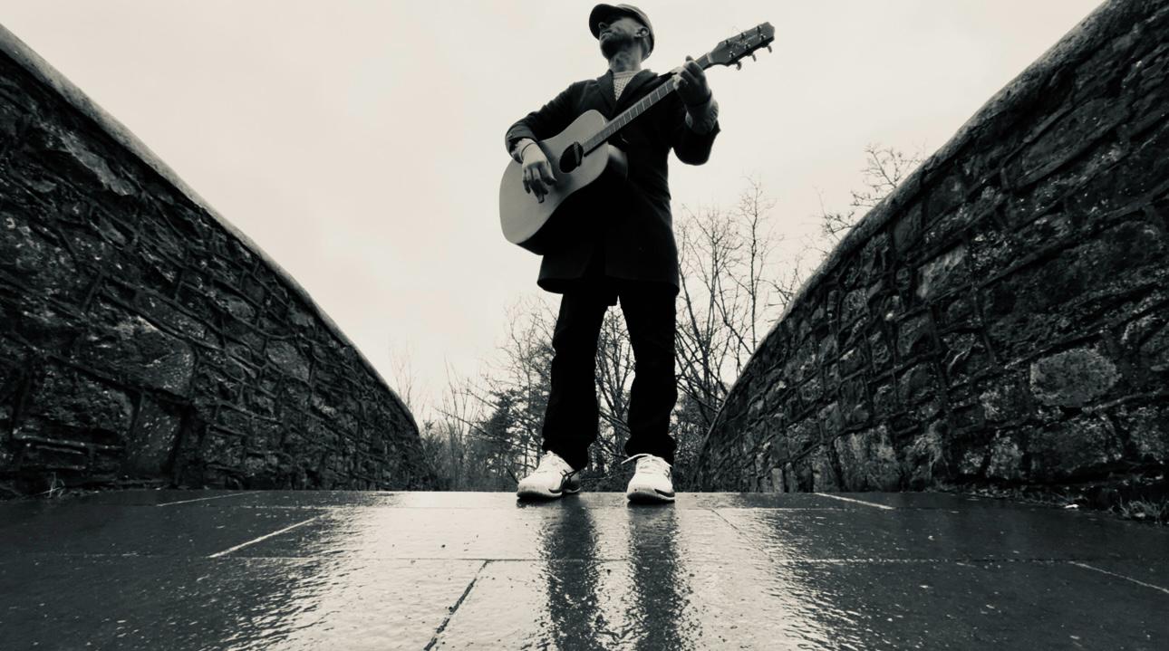 eoin standing on a bridge with a guitar facing the camera